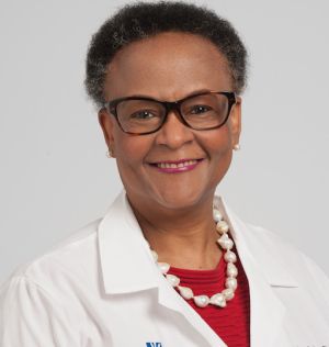 Mujer sonriente con una bata blanca pelo corto negro y canosoy gafas de ver