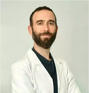 Hombre sonriente con una bata blanca, pelo corto castaño y barba muy poblada