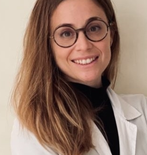 Mujer de mediana edad sonriente con gafas y pelo corto castaño con camiseta de médico blanca.