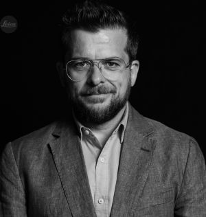 Hombre sonriente con una camisa y una chaqueta gris y gafas de ver